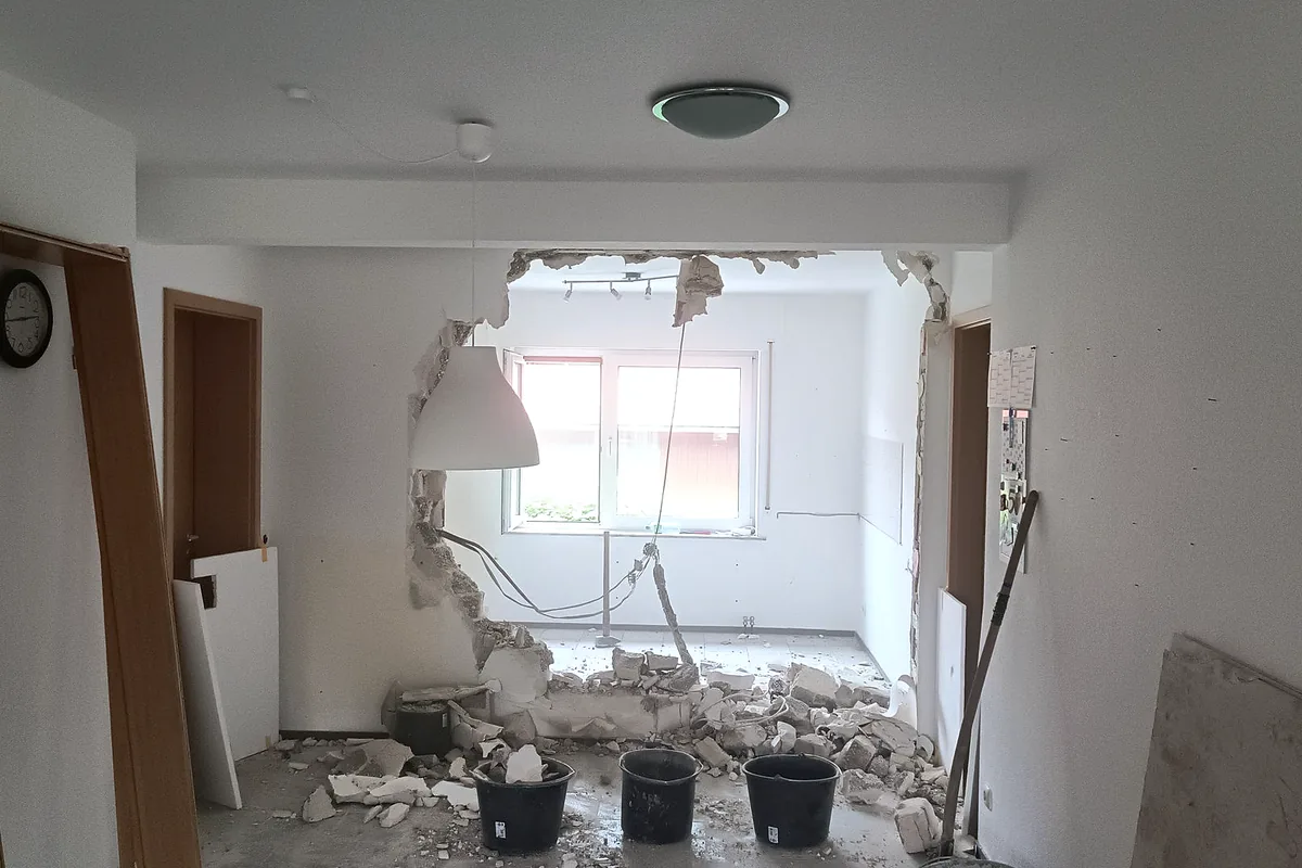 Geöffneter Wanddurchbruch zwischen zwei Räumen, daneben die Eimer für den Bauschutt