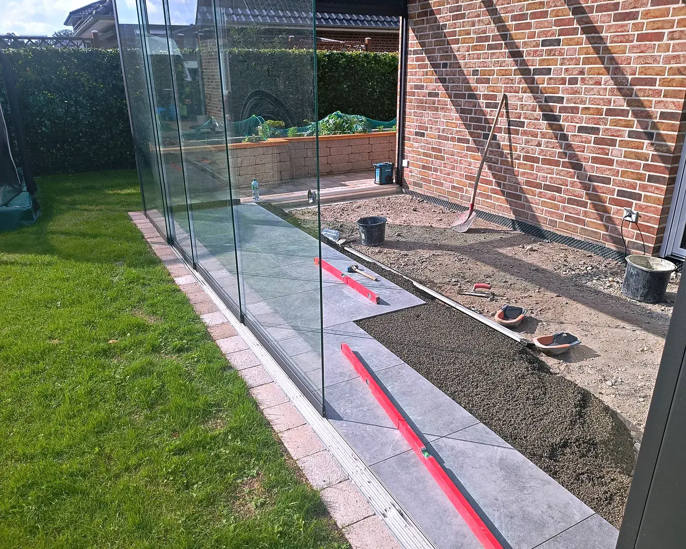 Verlegung der Großformatplatten entlang der Glasschiebewand, daneben das Bett aus Drainagemörtel