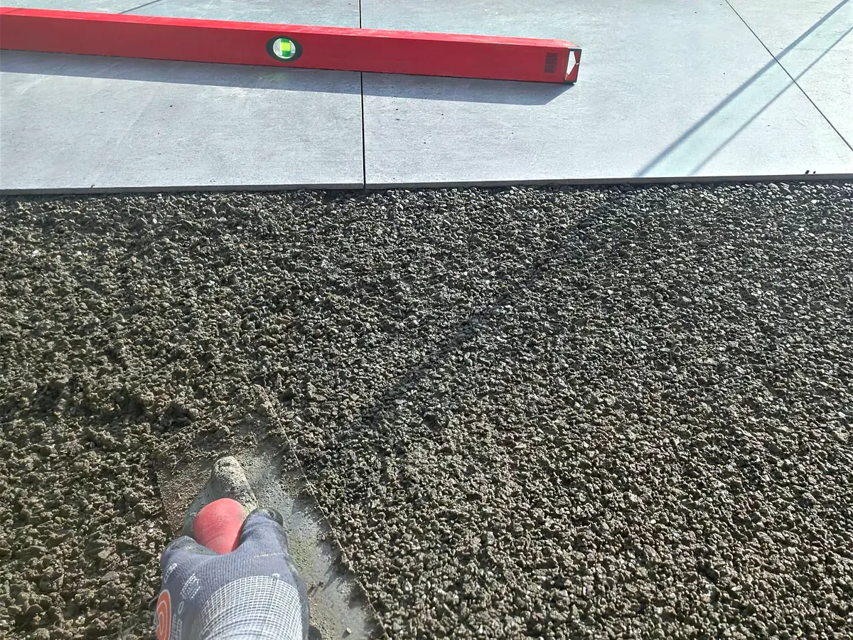 Drainagemörtel wird mit der Kelle abgezogen, dahinter die gesetzten Großformatplatten mit der Wasserwaage