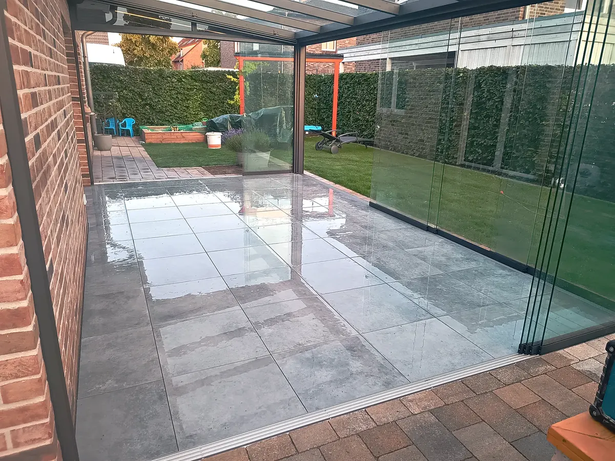 Fertige Terrasse mit Großformatplatten unter dem Glasdach, Blick durch die Glaswände in den Garten