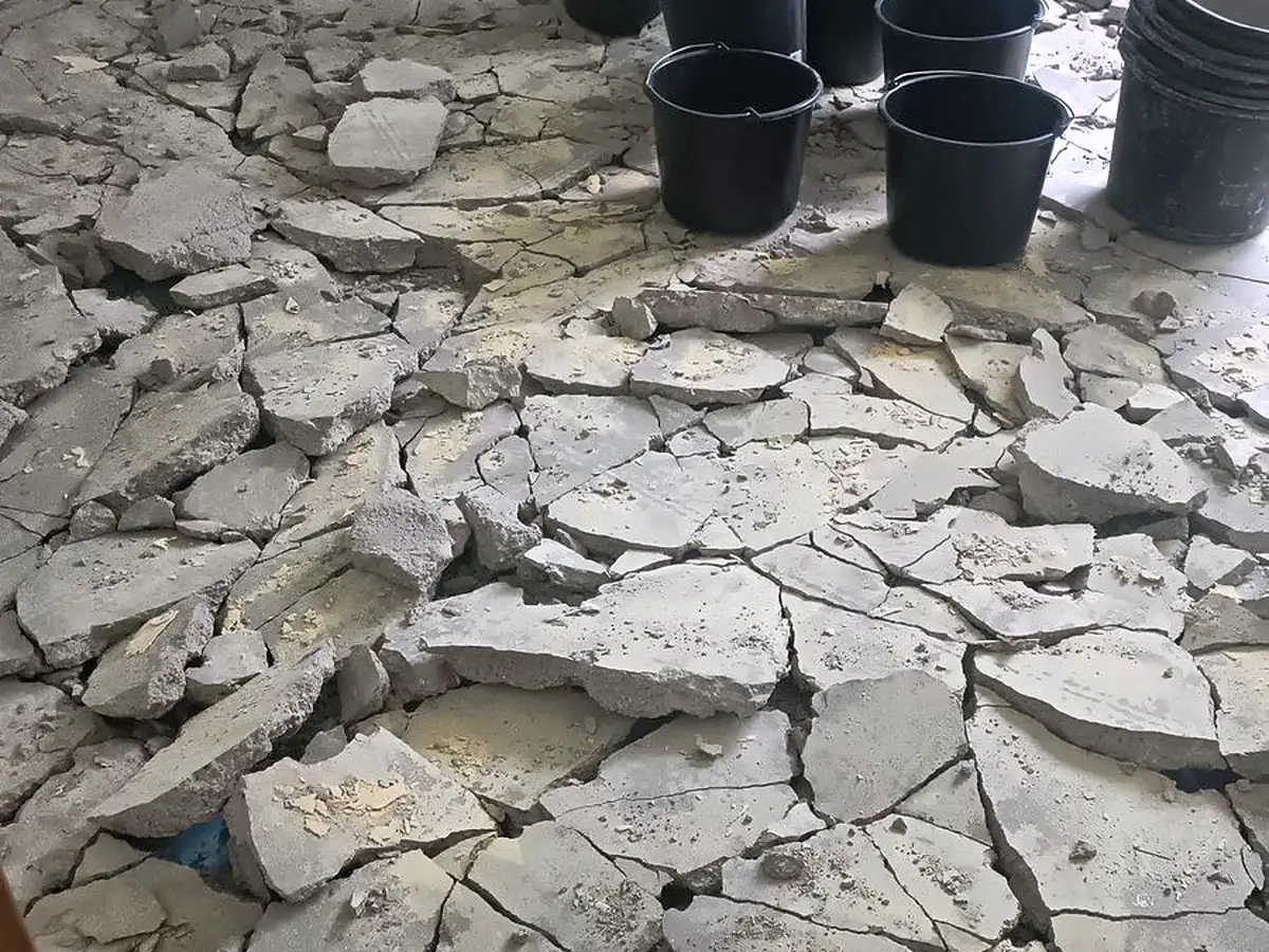 Aufgebrochener Estrich im Rückbau, Bruchstücke und Eimer auf dem Rohboden